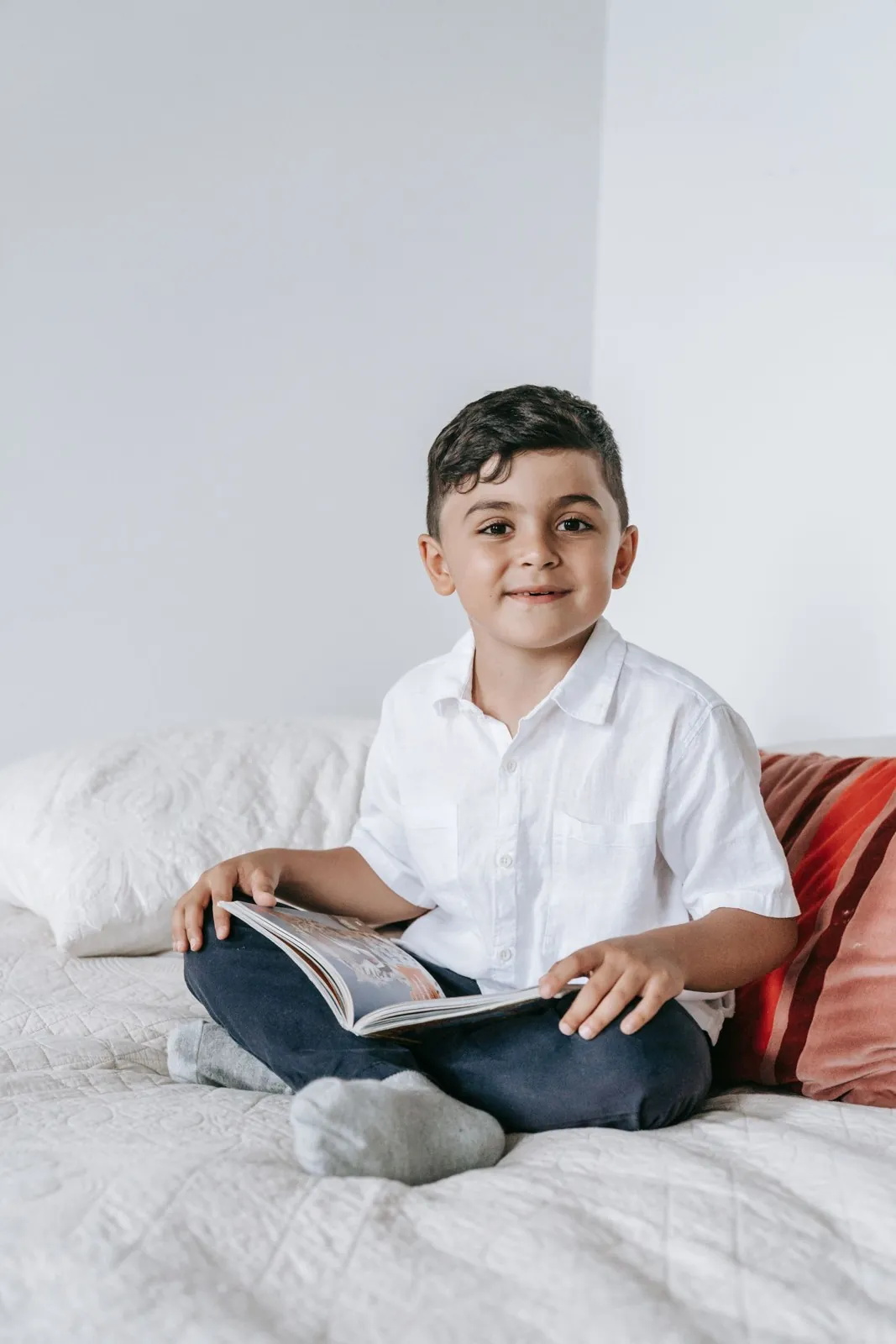 Niño sonriente lee un libro sentado en su cama