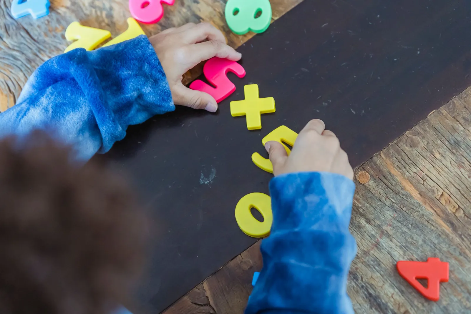 Manos de un niño arman una suma con números de goma de colores sobre una mesa de madera