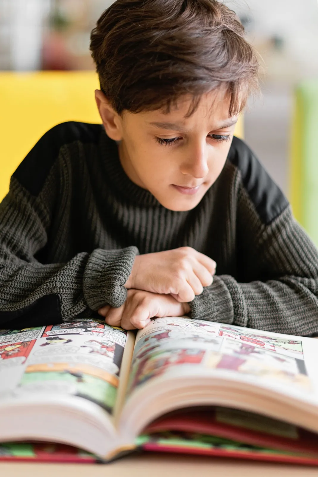 Niño con chaleco verde lee con atención un libro de colores